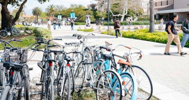 An image of bicycles stacked in a rack, with two male students walking past on the Santa Barbara campus.