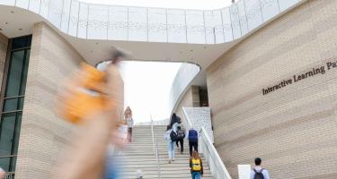 People moving through the University of California, Santa Barbara Interactive Learning Pavilion, with stairs leading between curved brick walls and open-air walkways.