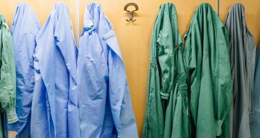 Surgical gowns in shades of green, blue, and gray hanging on hooks in a hospital changing area.