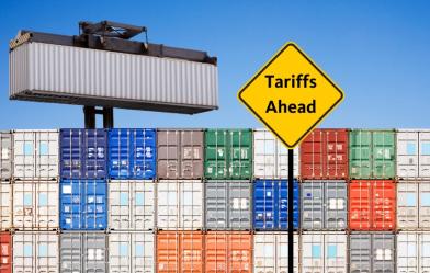 A picture of shipping containers with a yellow sign that reads "Tariffs Ahead"