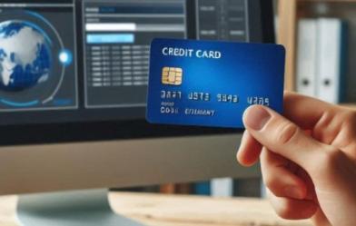hand holding a credit card in front of a monitor
