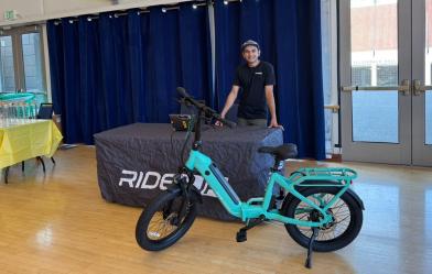 A student stands at a display table behind an e-bike