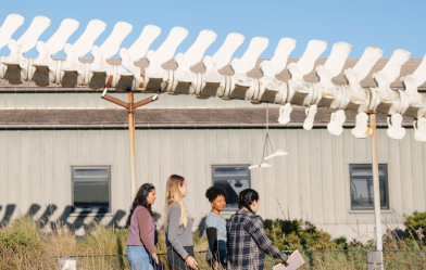 Students walking past a building under a large dinosaur spine model