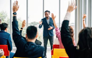 Presenter leads an interactive workshop as several participants raise their hands.