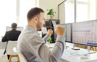 Office employee celebrates while reviewing information on a computer monitor.