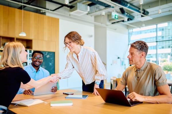 Four people at a conference table. Two are shaking hands.