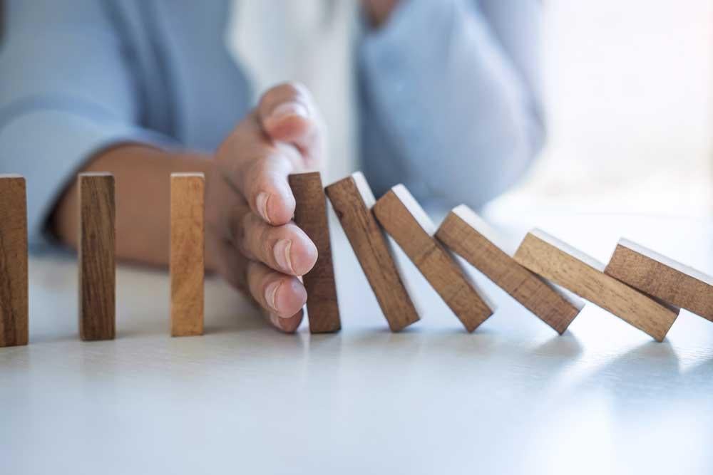 A hand blocking a set of dominos from falling