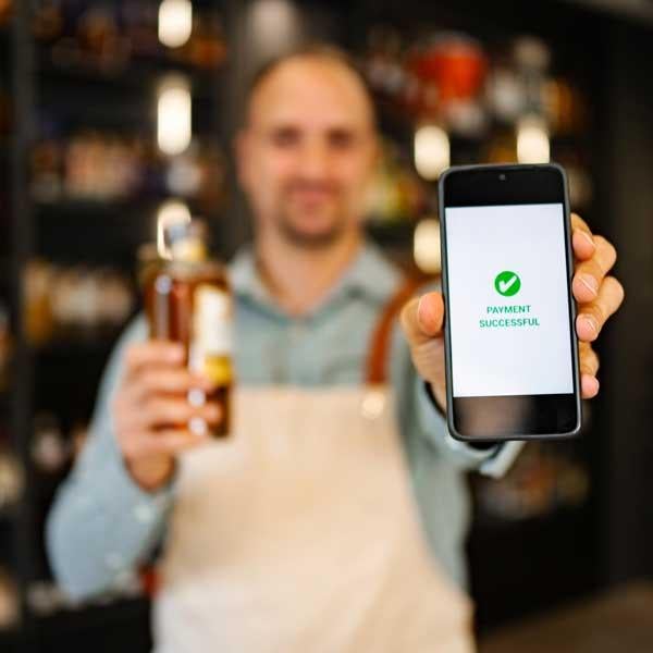 A man holding a bottle of alcohol in one hand, his other hand is showing a payment confirmation on his phone 